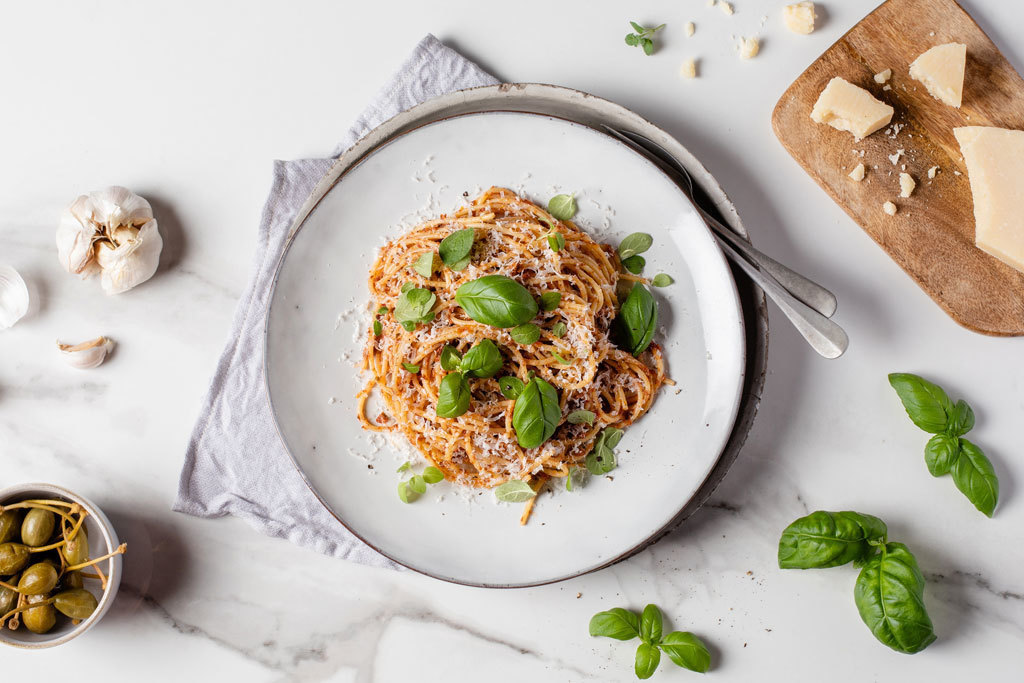 Maukasta tapenade-pastaa vaalealla lautasella koristeltuna basilikan lehdillä