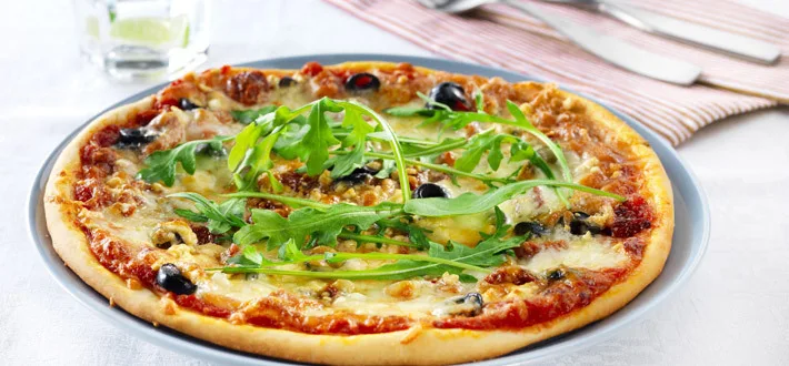 Herkullinen kolmen juuston pizza lautasella koristeltuna rucolalla