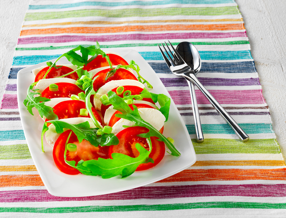 Perinteinen tomaatti-mozzarellasalaatti koristeltuna rucolalla ja kevätsipulilla